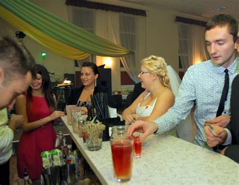 Zdjęcie uśmiechniętych barmanów przygotowujących kolorowe koktajle na tle weselnej sali