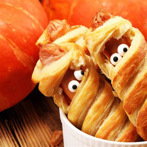 Ilustracja przedstawiająca różnorodne przekąski na Halloween: mumie z parówek, jabłkowe potwory, dyniowe muffiny.