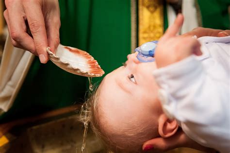 Zdjęcie dziecka podczas ceremonii chrztu świętego z zapaloną świecą i szatką.