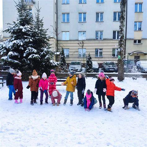 Grupa przedszkolaków lepi bałwana na śniegu.