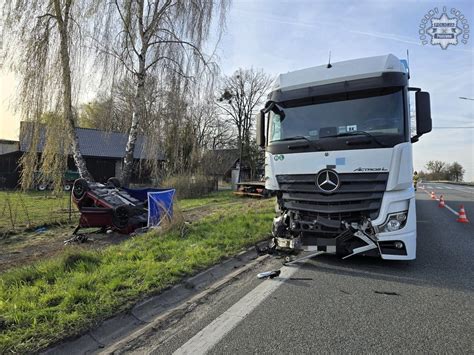 zdjęcie z miejsca wypadku drogowego z widocznym rozbitym samochodem i pracującymi na miejscu służbami ratowniczymi