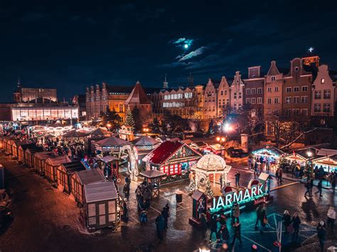 Ilustracja przedstawiająca tłoczny jarmark bożonarodzeniowy w Berlinie, z widocznymi straganami, choinkami i ludźmi spacerującymi wśród świateł.