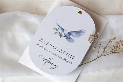 Ilustracja przedstawiająca owalne zaproszenie komunijne z błękitnym gołąbkiem w technice akwareli.