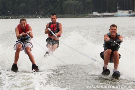 Ilustracja przedstawiająca grupę młodych ludzi bawiących się na nartach wodnych i wakeboardzie na tle jeziora.