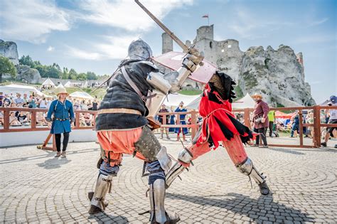 Schematyczny rysunek przedstawiający średniowieczny turniej rycerski z widownią i walczącymi rycerzami