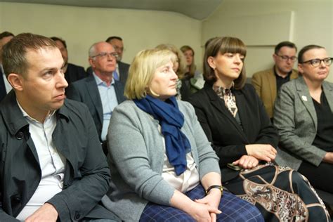 Grupa uczestników balu charytatywnego w eleganckich strojach, rozmawiająca przy stolikach.
