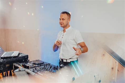 Zdjęcie DJ-a z mikrofonem i konsolą DJ-ską na tle rozbawionych gości weselnych.