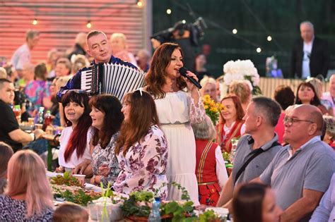 Zdjęcie akordeonisty grającego podczas weselnej biesiady przy stołach, z uśmiechniętymi gośćmi w tle.