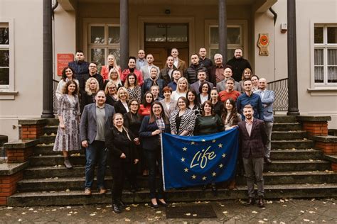 Grupa osób pozuje do zdjęcia przed budynkiem, wśród nich są przedstawiciele władz i organizacji.