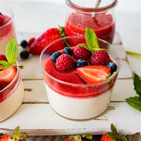 Kolorowe i apetyczne panna cotta w szklanych pucharkach, ozdobione świeżymi owocami i listkiem mięty.