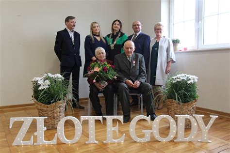 Fotografia przedstawiająca parę seniorów podczas uroczystości Złotych Godów, z widocznym tortem i kwiatami.